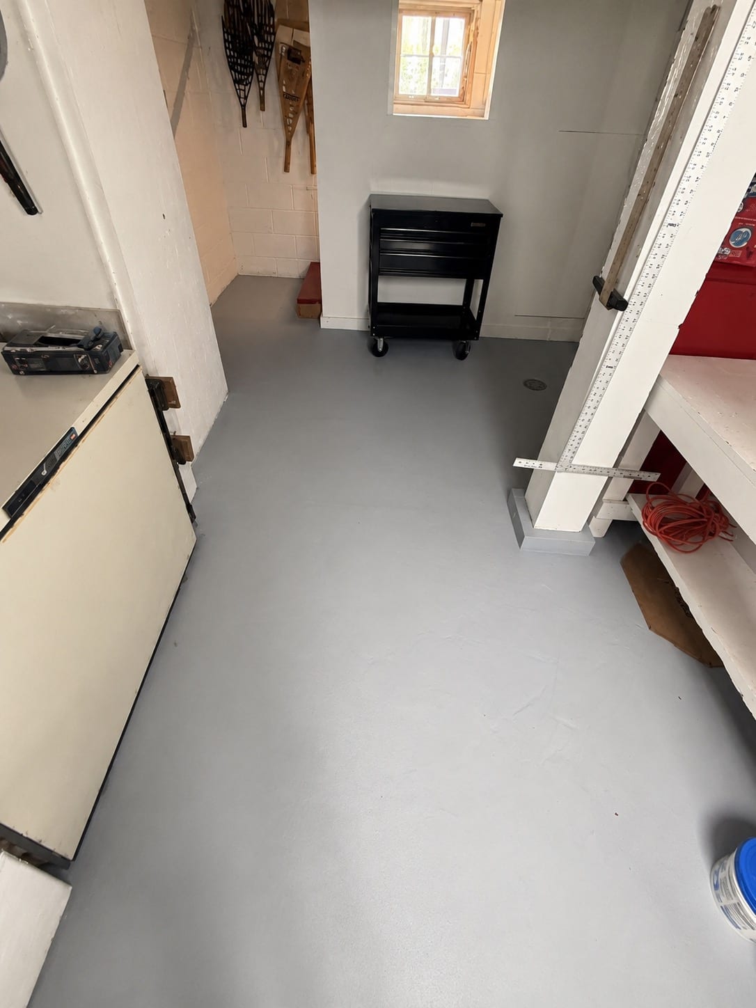A basement workshop corner with an even gray floor coating running to the wall edges