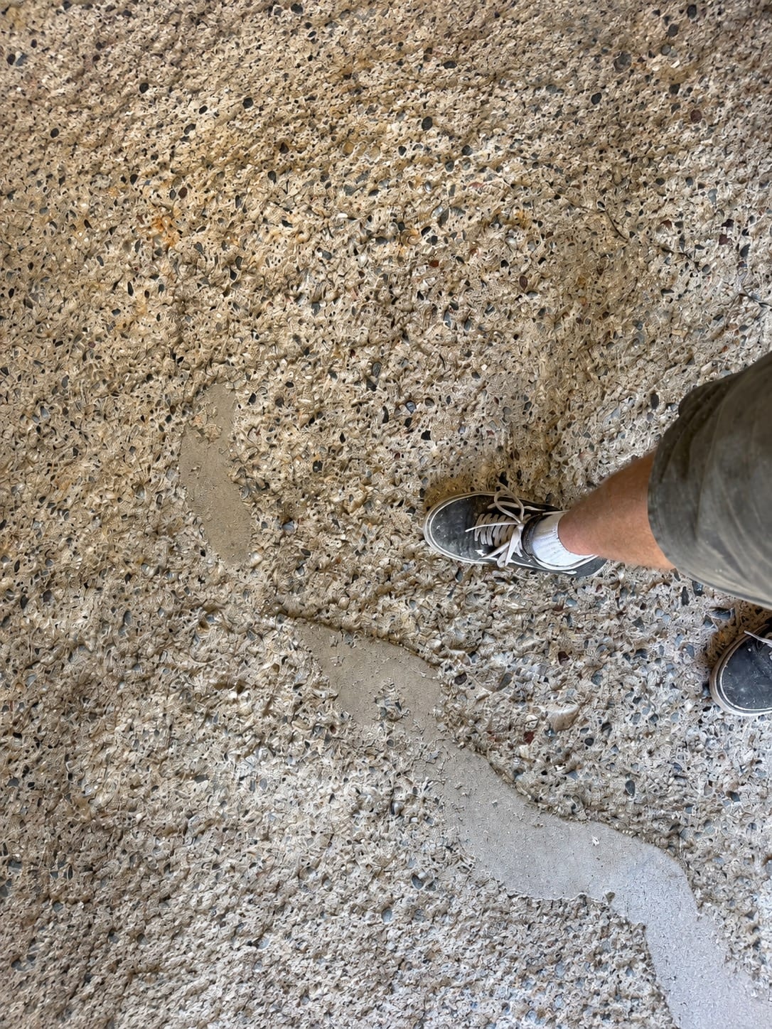 Close view of a badly spalled concrete slab with the surface broken away to expose loose aggregate, photographed from standing height